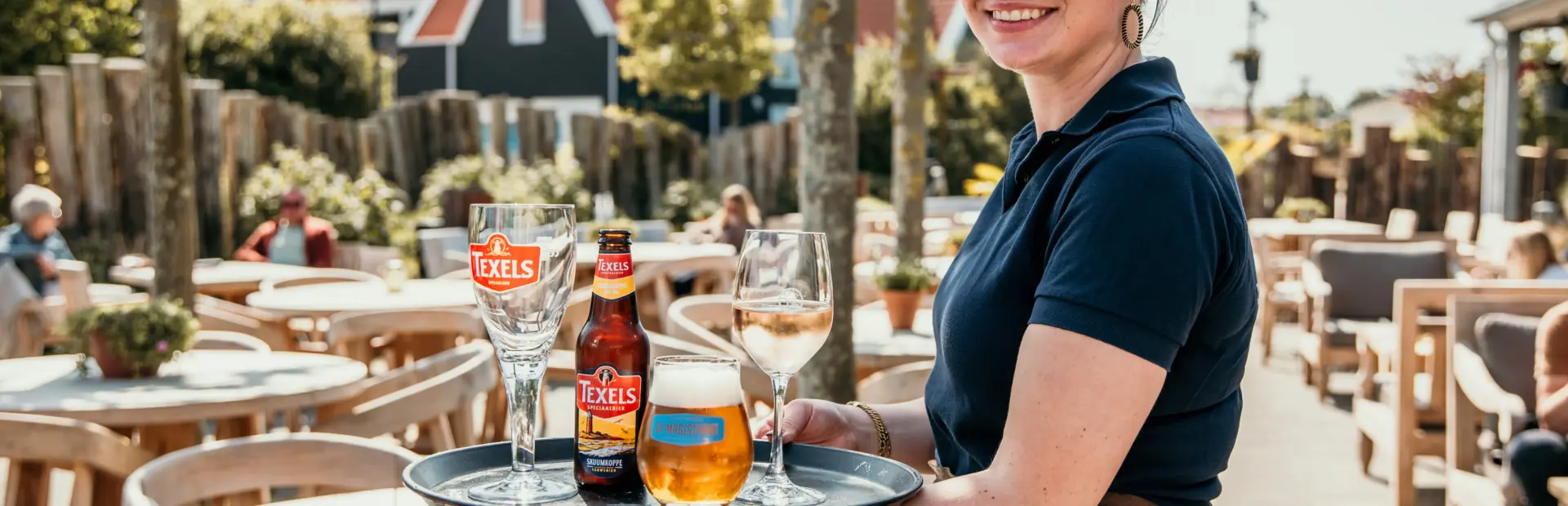 Gastvrije bediening op De Zeeuwse Kust, een vriendelijke serveerster brengt een koud glas Texels bier op het zonnige terras