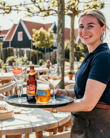 Gastvrije bediening op De Zeeuwse Kust, een vriendelijke serveerster brengt een koud glas Texels bier op het zonnige terras