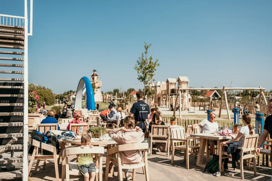 Gezellig terras bij De Zeeuwse Kust, ontspannen tafelen terwijl kinderen spelen op de avontuurlijke speelplaats