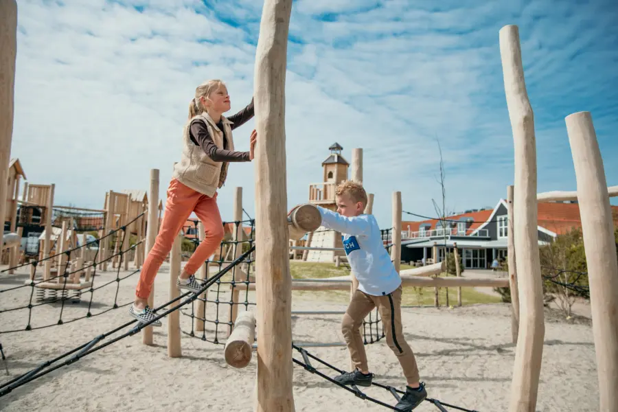 Twee kinderen klimmen in de nieuwe houten buitenspeeltuin 250 meter van het strand