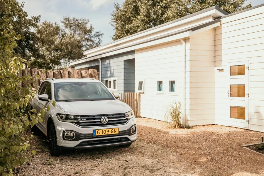 Geparkeerde auto bij een modern vakantiehuis op Strandpark De Zeeuwse Kust omringd door groen en natuurlijke elementen