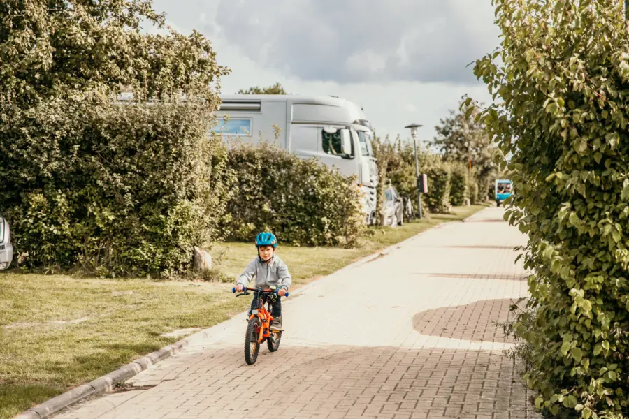 Kind fietst over een sfeervolle campingweg op Strandpark De Zeeuwse Kust omringd door groen met campers op de achtergrond