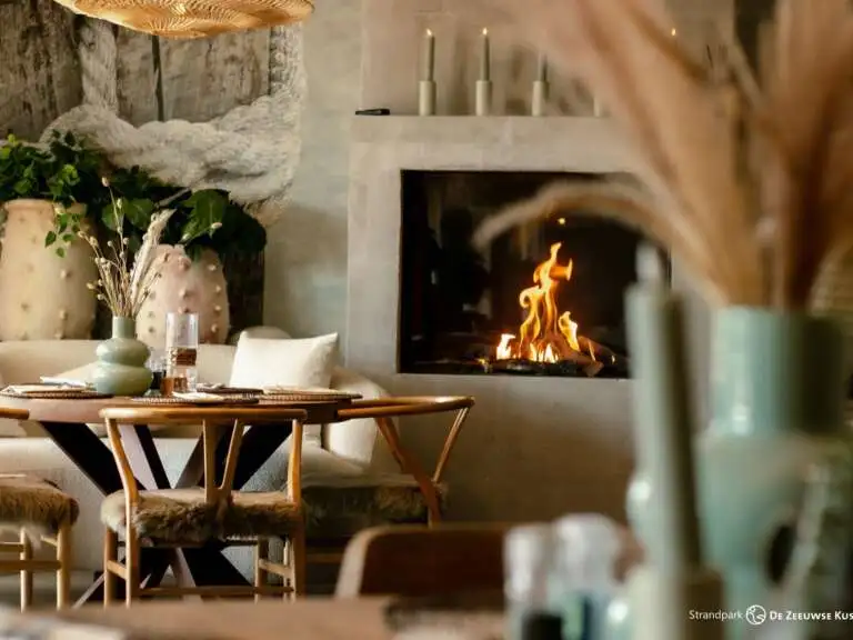 Gezellige eethoek met houten tafels in het restaurant van Strandpark De Zeeuwse Kust met een open haard
