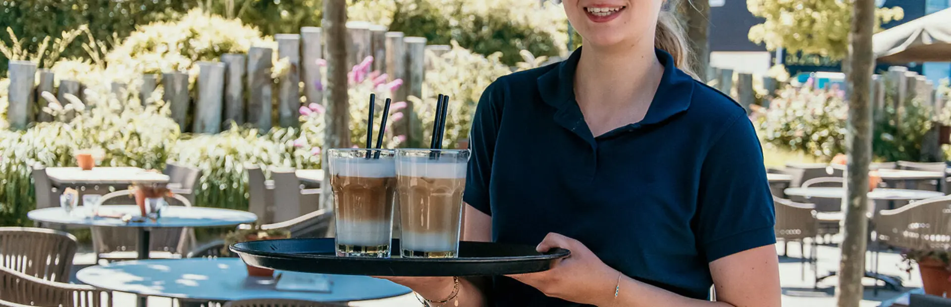 Een stralende serveerster brengt verse ijskoffies op een zonnig terras. Genieten maar