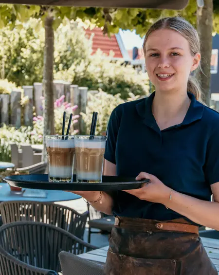 Een stralende serveerster brengt verse ijskoffies op een zonnig terras. Genieten maar