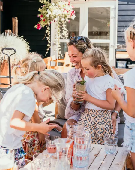 Een zonnig terras, lachende kinderen en een moeder die geniet van het moment bij Strandpark De Zeeuwse Kust