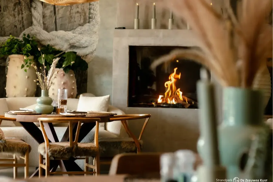 Gezellige eethoek met houten tafels in het restaurant van Strandpark De Zeeuwse Kust met een open haard