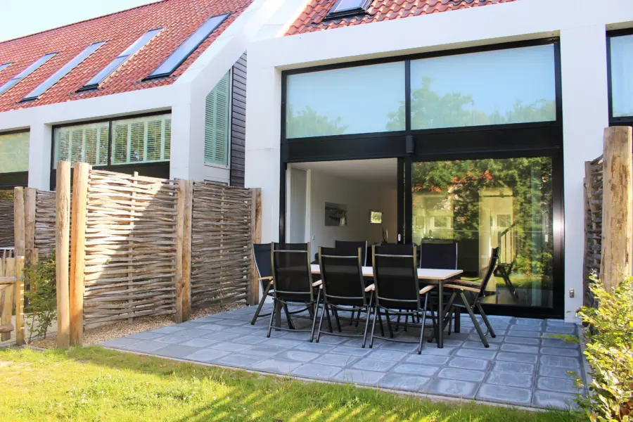 Ruim terras van een Duinhus vakantieaccommodatie op Strandpark De Zeeuwse Kust met een grote eettafel omringd door groene natuur en natuurlijke schuttingen